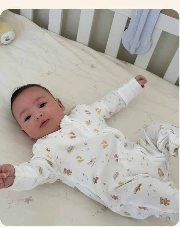 Baby wearing a Peach and Pebble organic cotton romper in a cot
